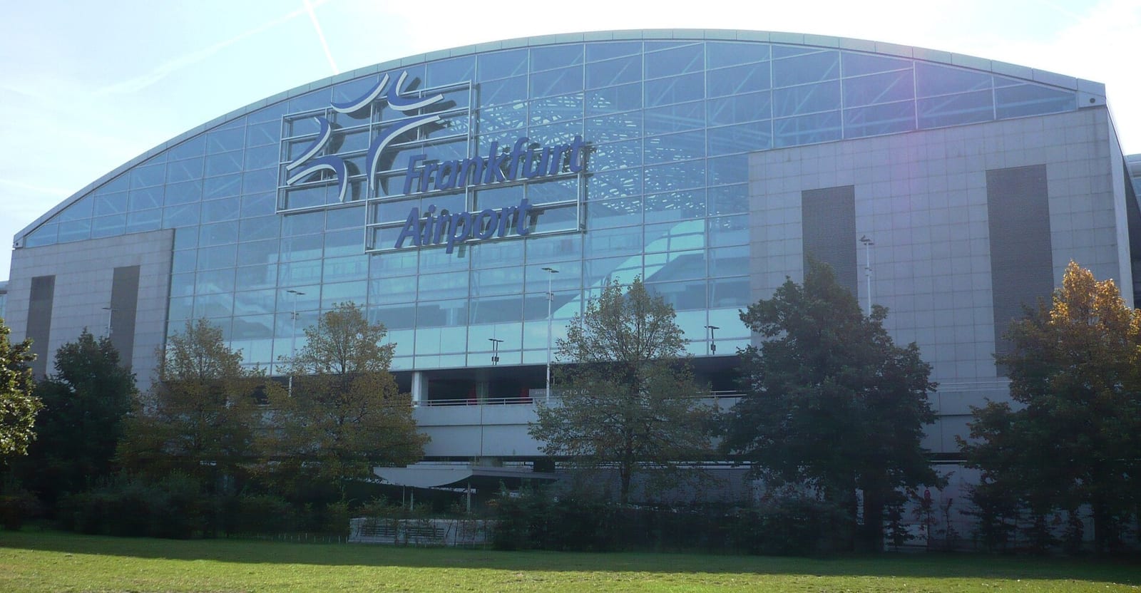 Frankfurt Airport's Terminal 2 building, its glass facade catching afternoon light behind a row of trees