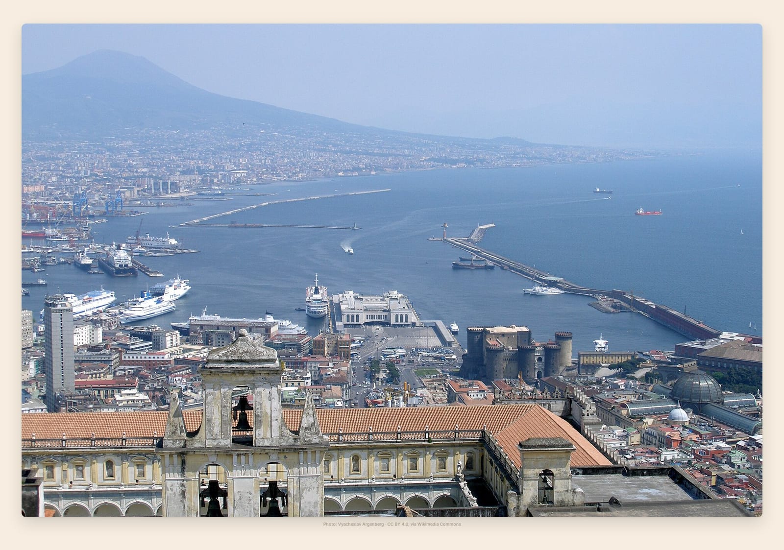 Naples' packed waterfront curves beneath Vesuvius, ferries and cruise ships filling the bay below