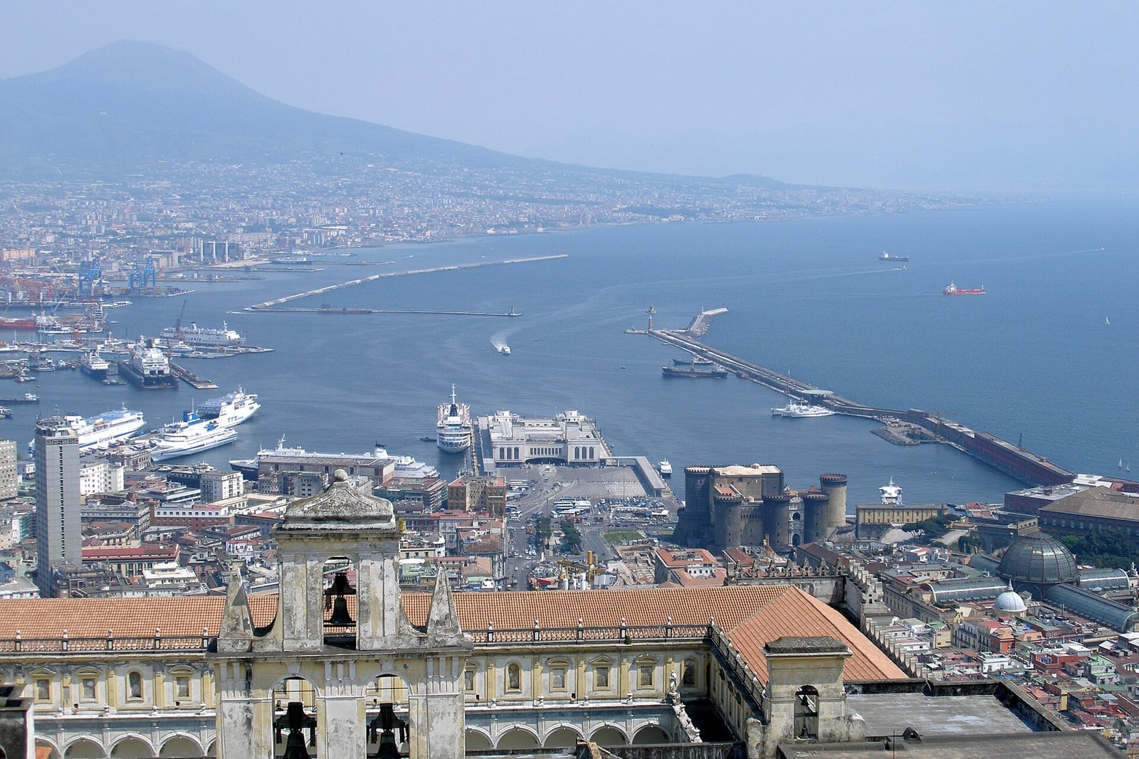 Naples' packed waterfront curves beneath Vesuvius, ferries and cruise ships filling the bay below