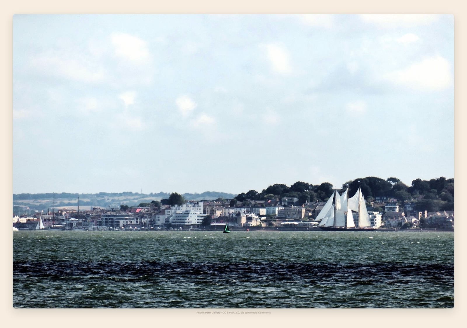 A tall ship under full sail crosses the Solent in front of Cowes' waterfront