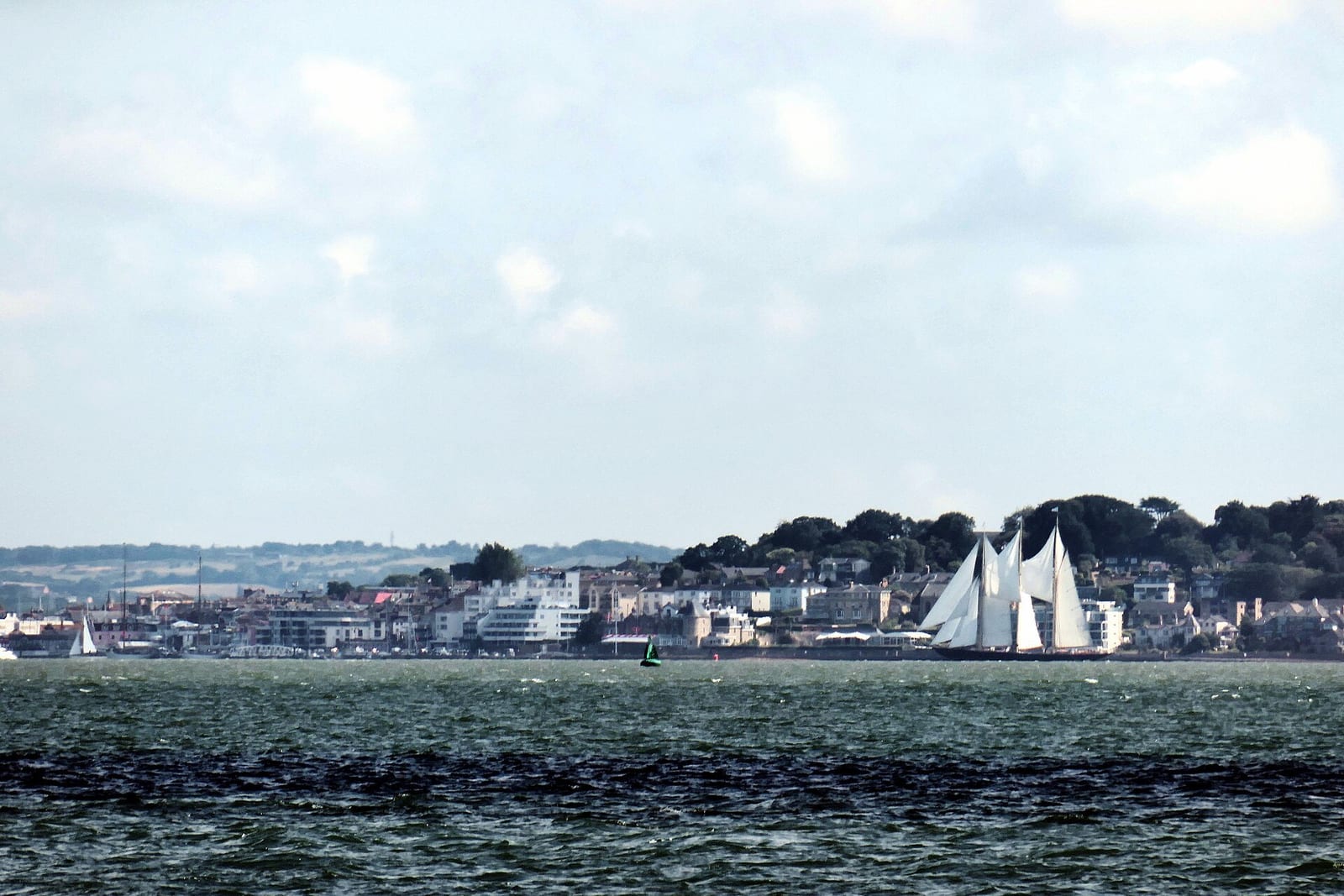 A tall ship under full sail crosses the Solent in front of Cowes' waterfront