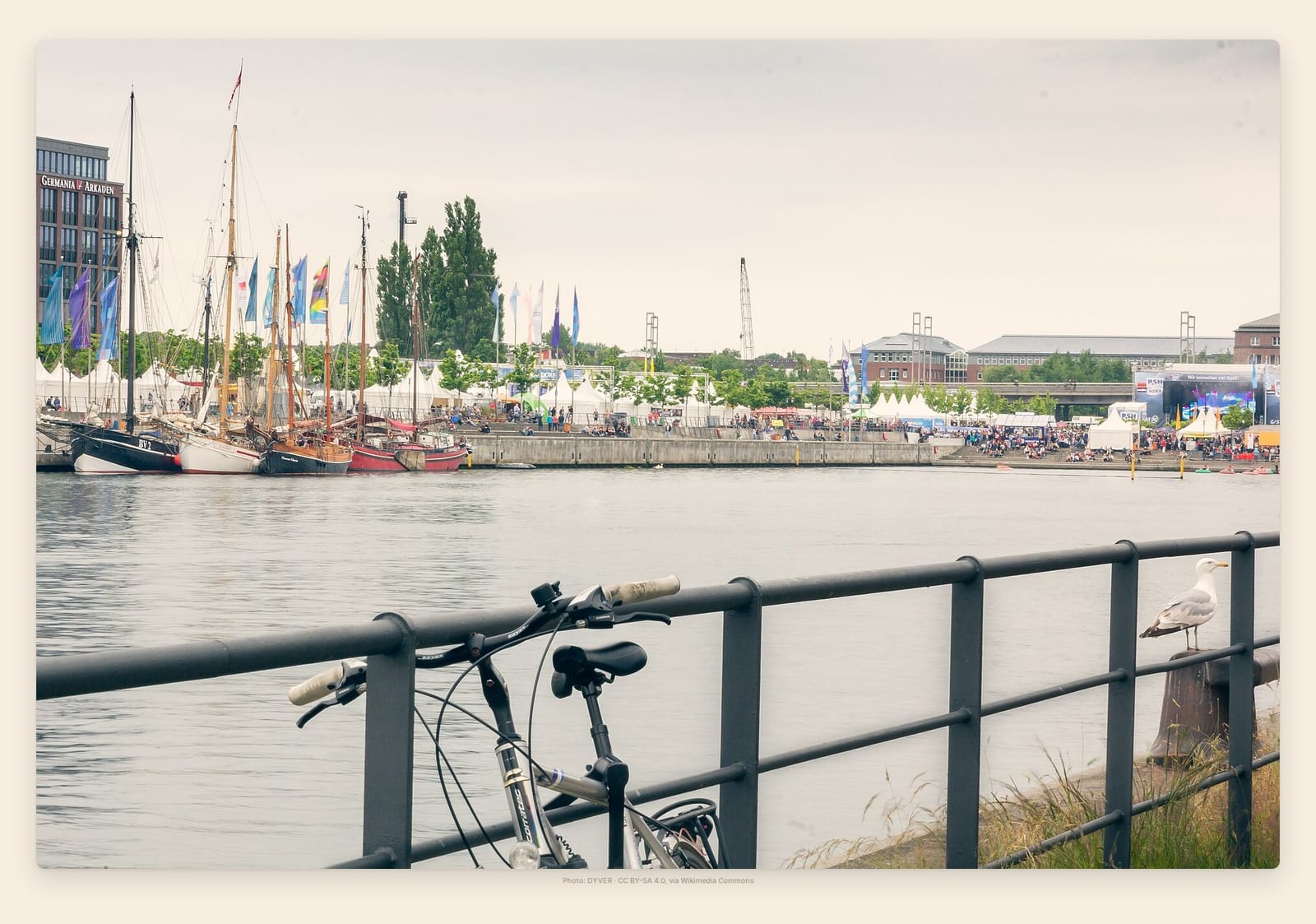 Traditional tall ships moored in Kiel's Hörn harbor as crowds fill the quay during Kiel Week