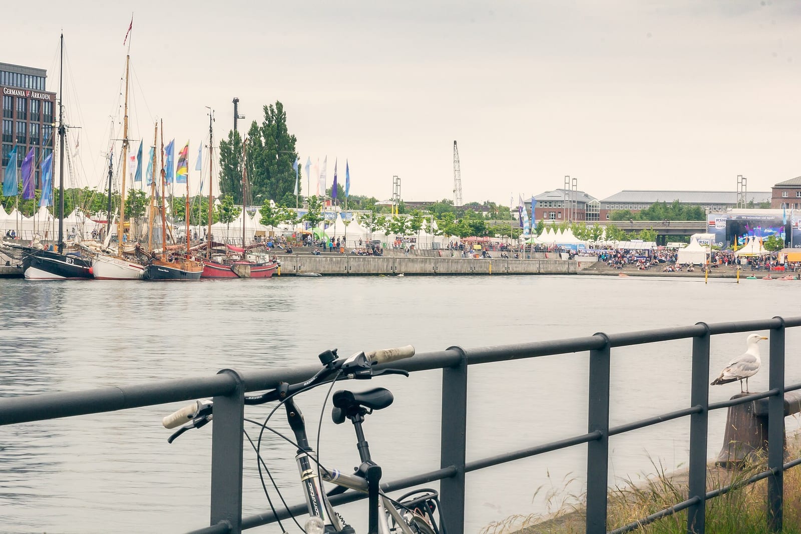 Traditional tall ships moored in Kiel's Hörn harbor as crowds fill the quay during Kiel Week