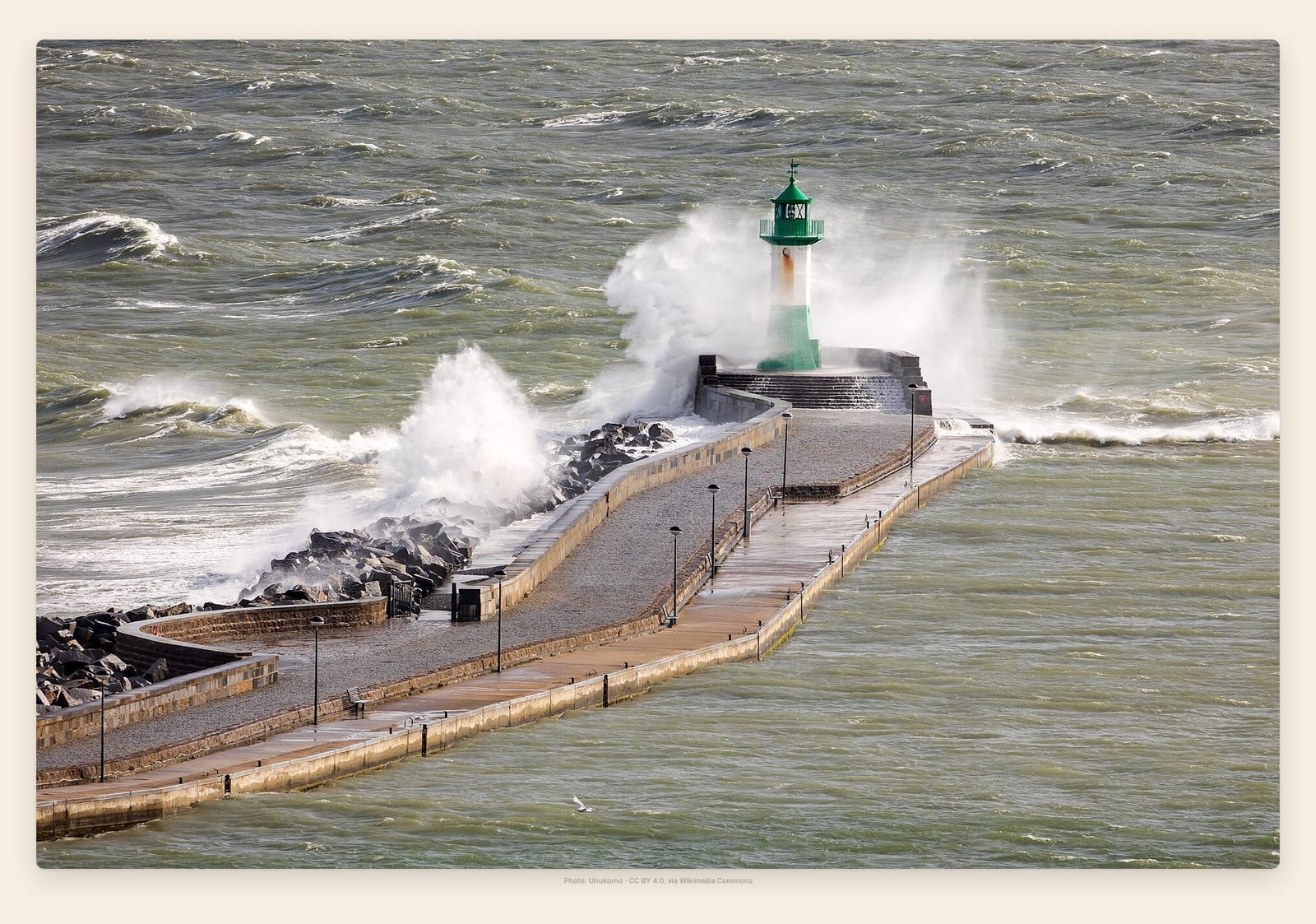 Waves break over Sassnitz's harbor mole and its green-and-white lighthouse on the Baltic