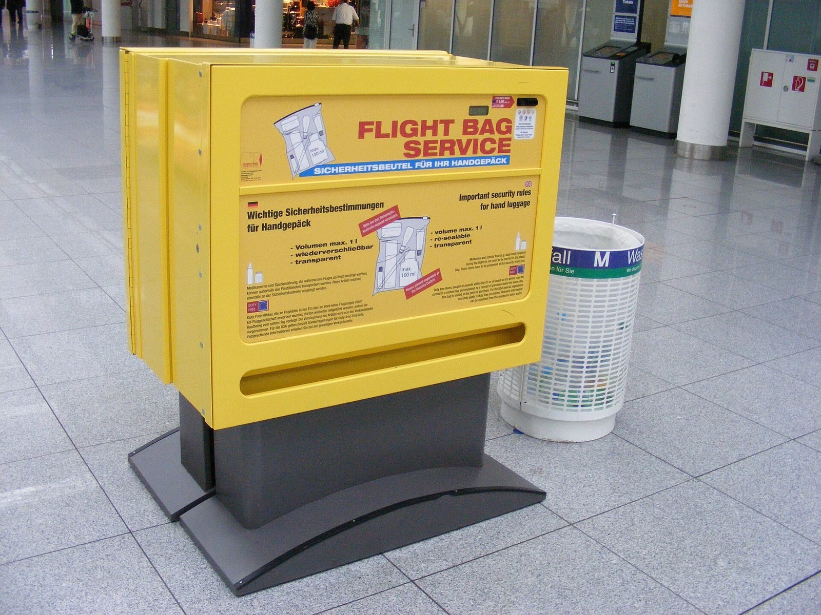 A yellow kiosk dispensing resealable plastic bags for hand luggage liquids at a German airport