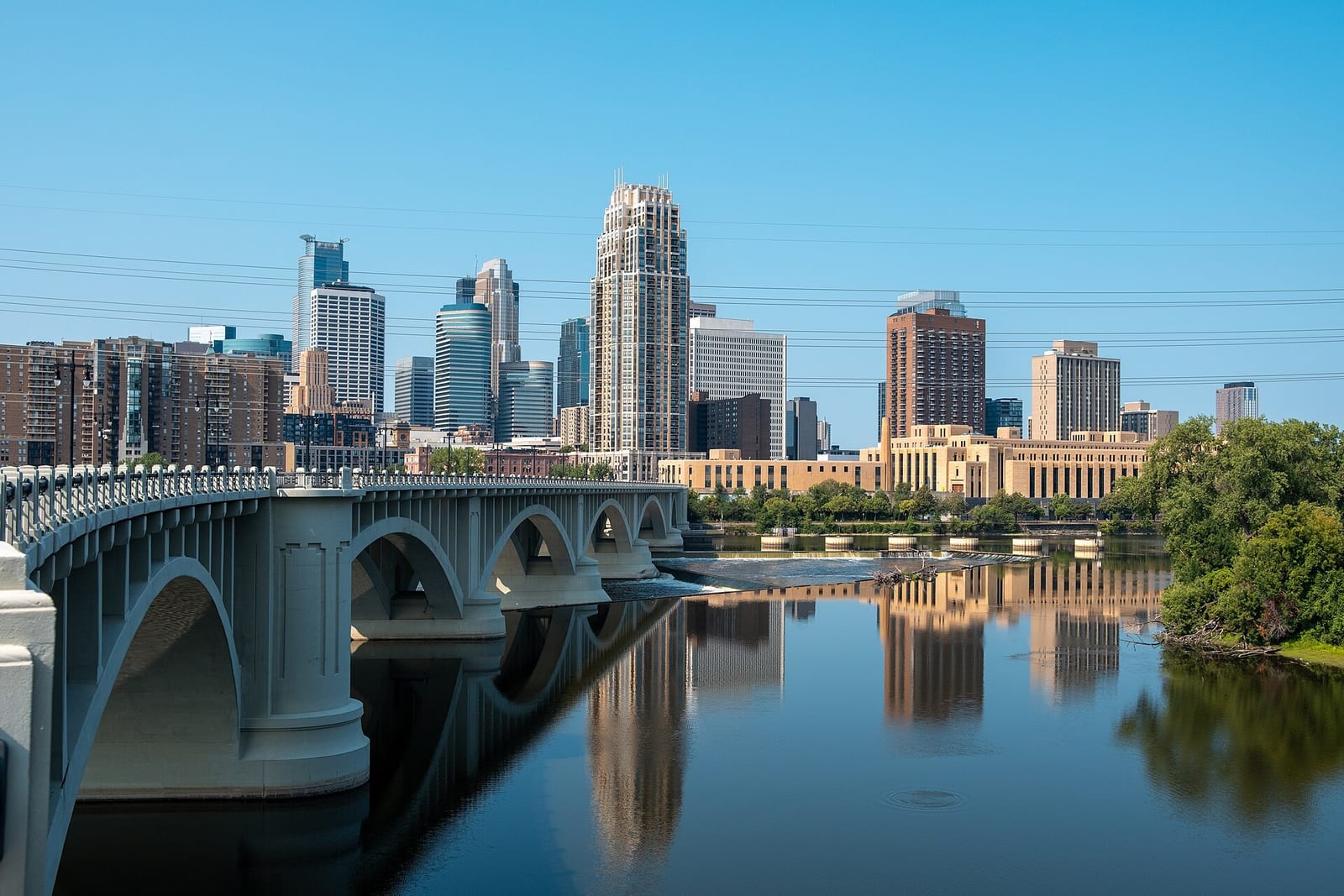 Downtown Minneapolis rises above the Mississippi River on a bright afternoon.