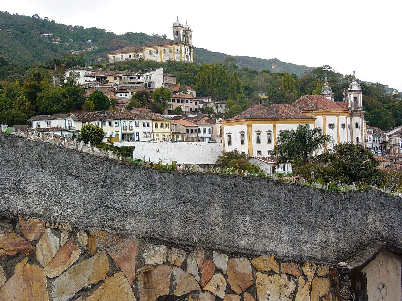 Ouro Preto's pastel townhouses and twin-towered baroque church climb a green hillside above a stone wall