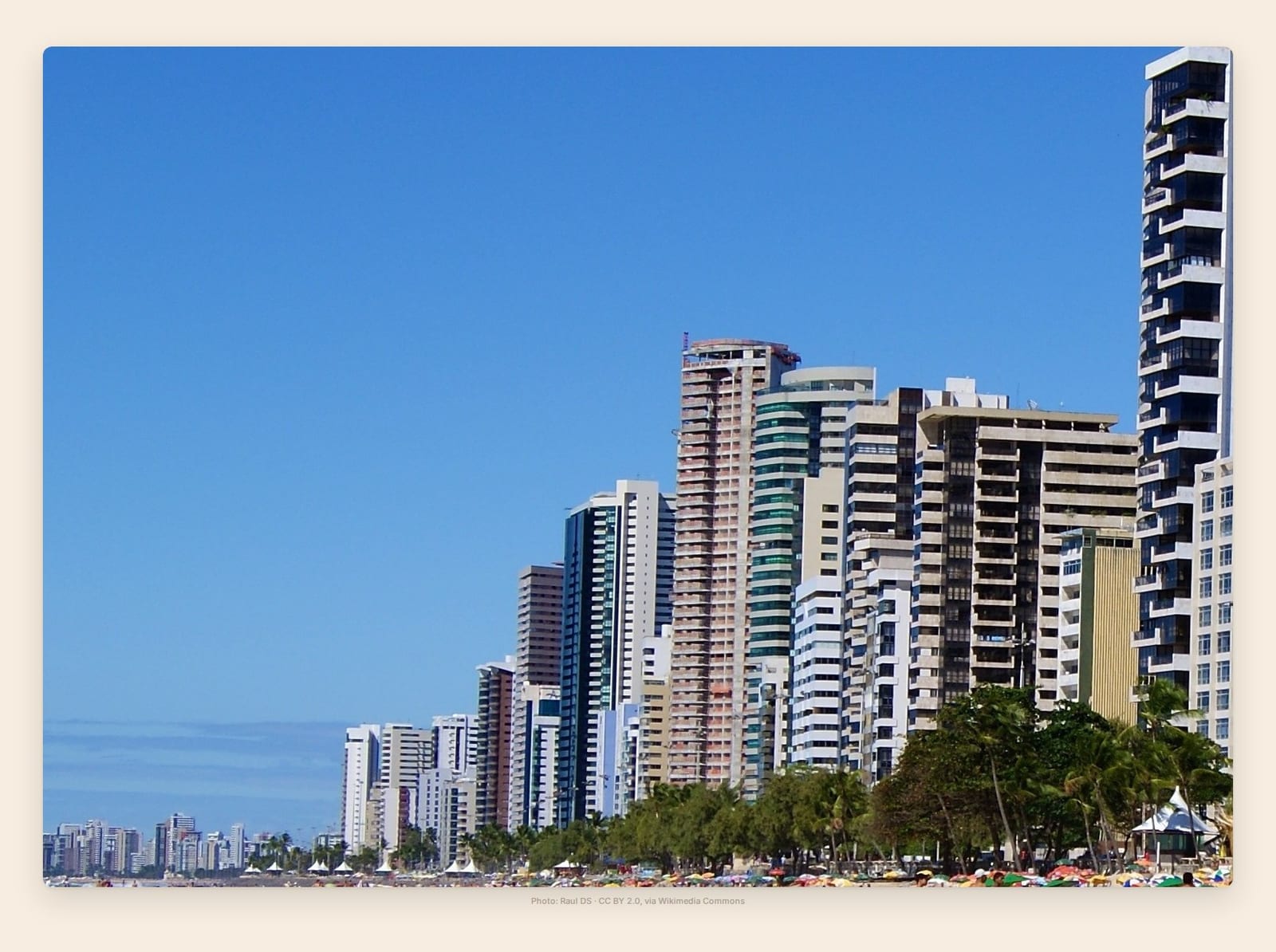 A dense wall of beachfront towers rises directly behind Boa Viagem's sand and striped umbrellas in Recife