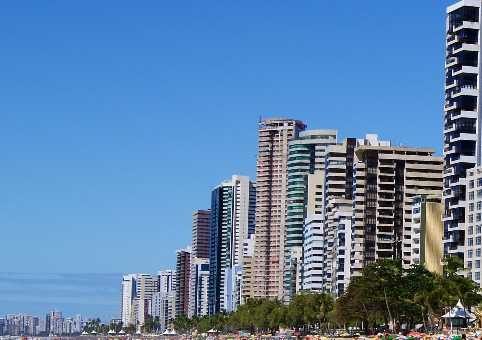 A dense wall of beachfront towers rises directly behind Boa Viagem's sand and striped umbrellas in Recife