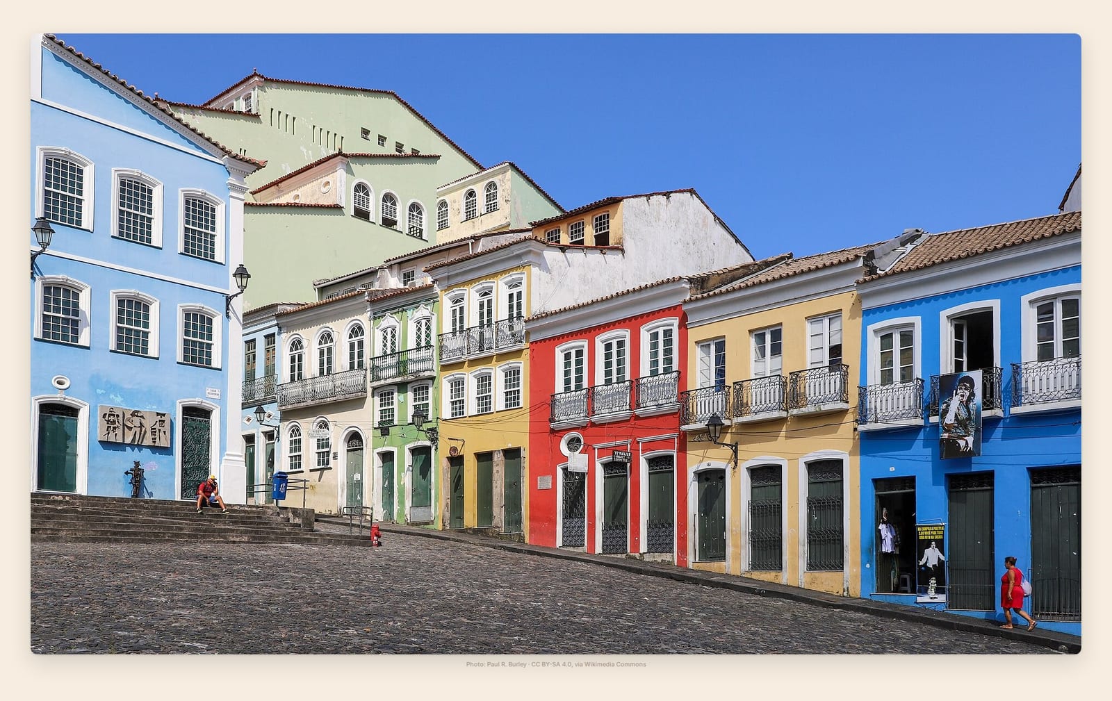 A row of blue, ochre and red colonial townhouses lines Pelourinho's steep cobblestone plaza in Salvador