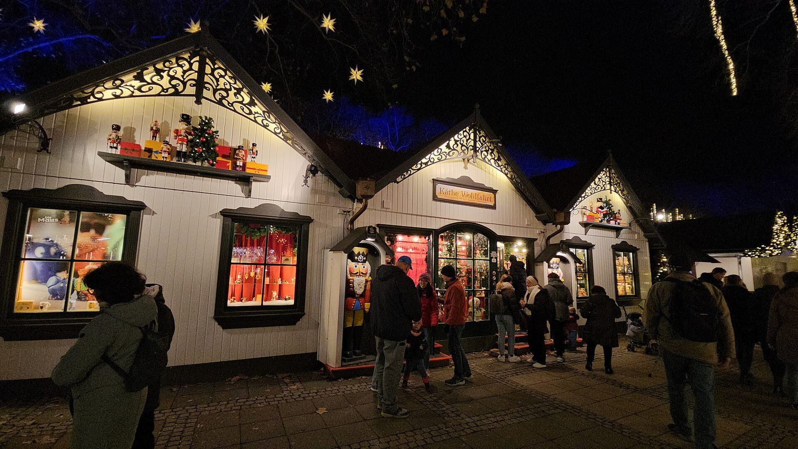 White wooden market cottages trimmed with nutcrackers and lights, shoppers browsing after dark