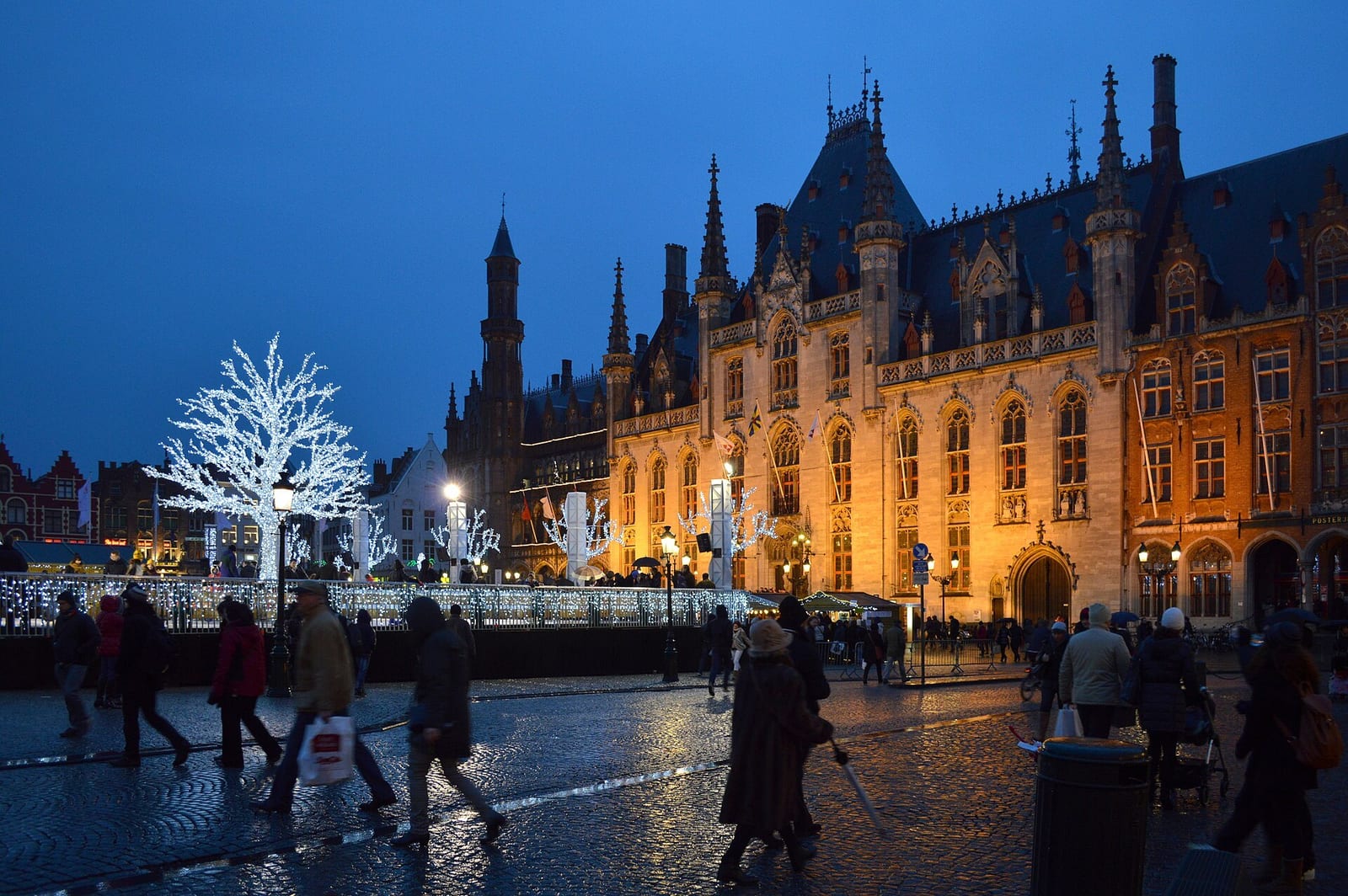 Bruges Markt square at dusk with lit white trees and a floodlit Gothic provincial court