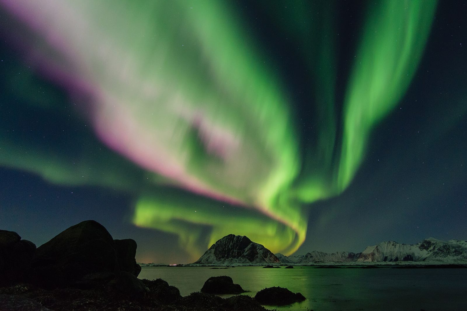 Green and violet aurora curtains ripple above snow-dusted peaks and a still fjord