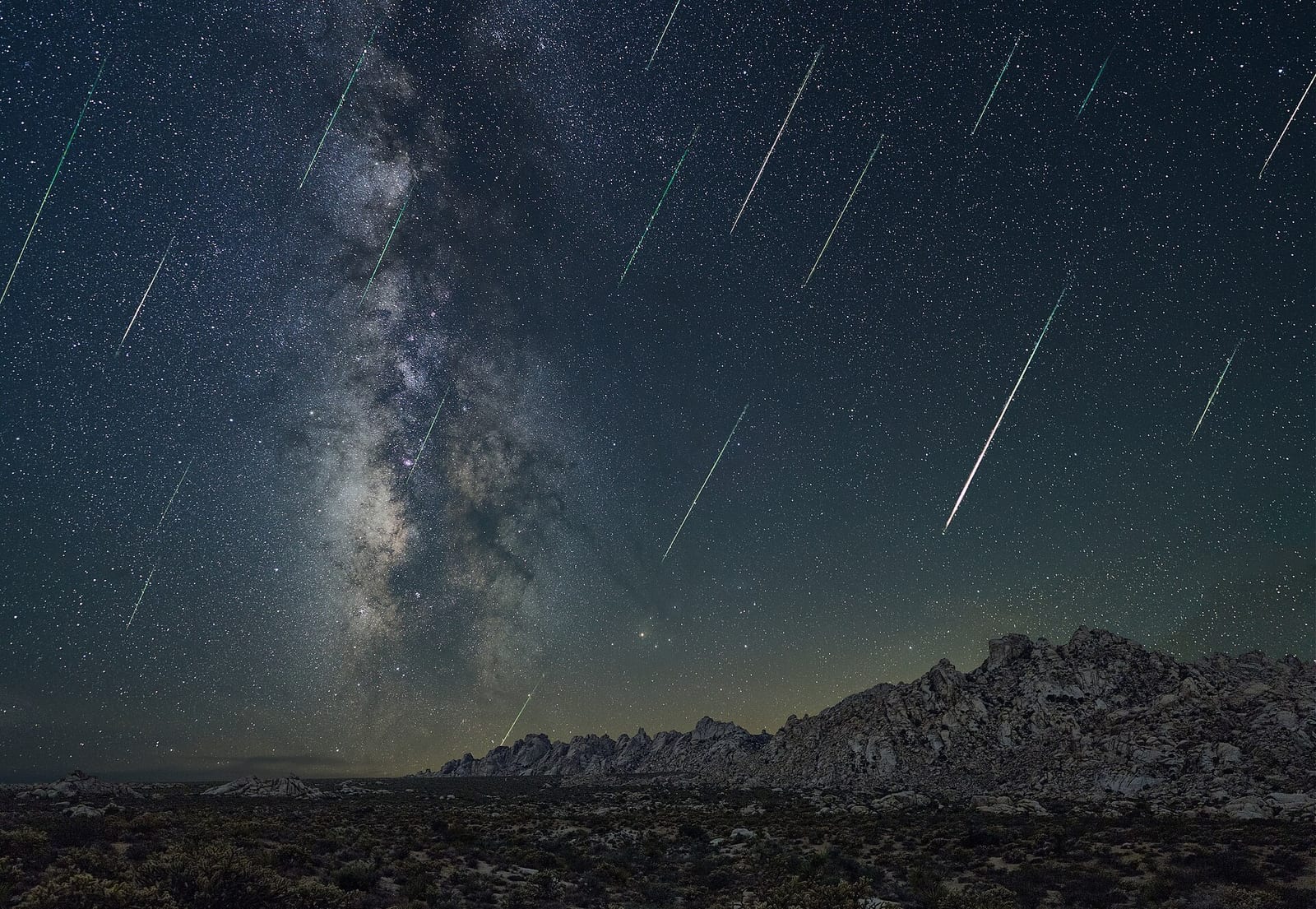 Dozens of Perseid meteors streak past the Milky Way above a desert mountain ridge