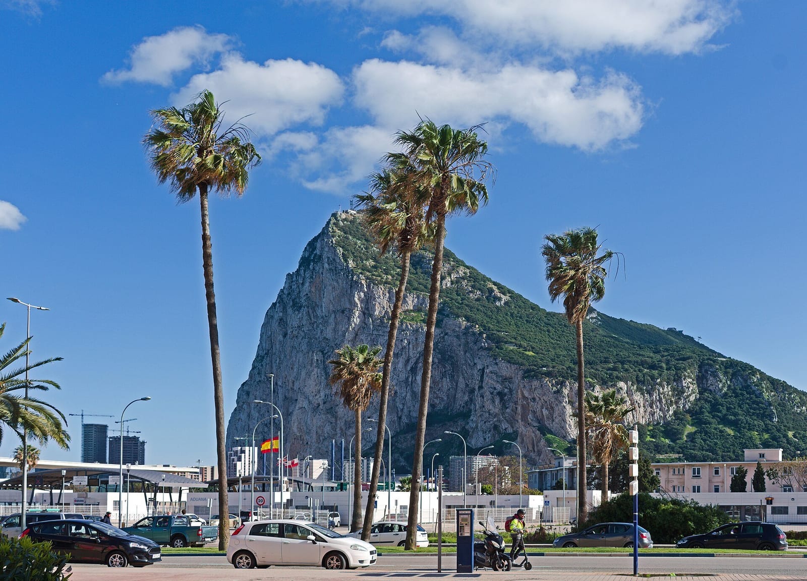 The Rock of Gibraltar rising behind palm trees on a La Línea avenue beside the border