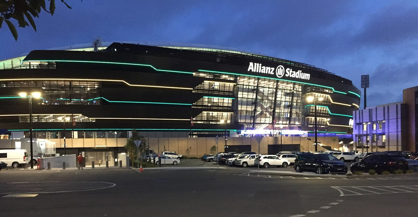 Allianz Stadium in Sydney lit up at dusk, its dark facade traced with green and gold lines