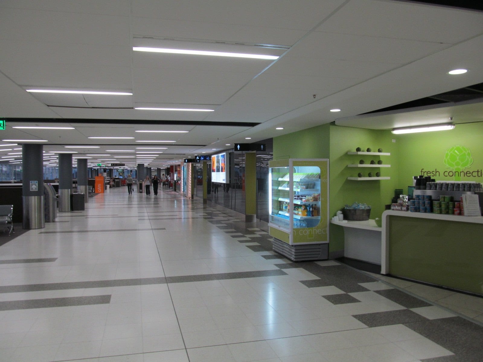 A wide, mostly empty concourse at Perth Airport, a few distant travellers walking past shopfronts