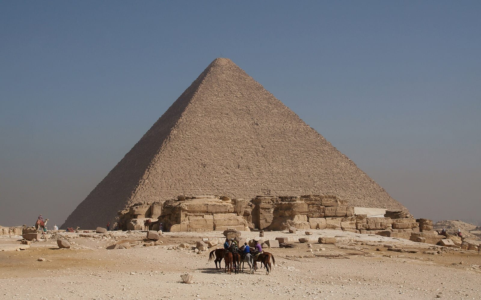 The Great Pyramid of Giza rising above the desert plateau, two camels crossing the sand below