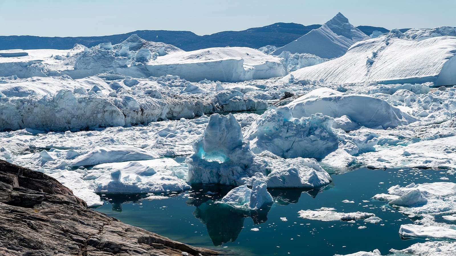 Icebergs calved from the ice sheet crowd the wide fjord beside Ilulissat, Greenland